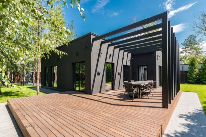 A wood deck with a pergola behind a dark house